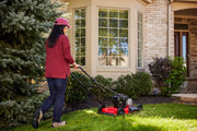 Photo of a person using a red Craftsman lawn mower, SKU CM11A-02T8793, on a front yard lawn near a house.
