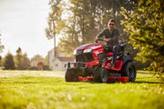 Photo of a red Craftsman riding lawn mower, SKU CM14AHA6ZMA93, on grass with trees and a house in background.
