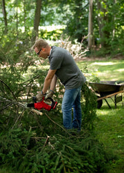 Photo of Craftsman CMCCS320D1 cordless chainsaw in use outdoors, cutting tree branches in a yard.