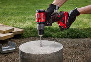 Photo of CRAFTSMAN cordless hammer drill CMCD726B drilling into concrete outdoors, held by gloved hands.