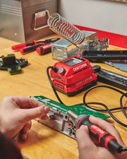 Photo of CRAFTSMAN CMCE040B soldering station with red and black body, used for circuit board work on a wood table.