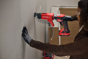 Photo of a person using a CRAFTSMAN CMCF600B cordless drywall screw gun with auto-feed, fastening drywall to a wall.