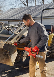 Person using CRAFTSMAN CMCGG001D1 cordless grease gun on construction equipment, wearing red gloves outdoors.