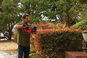 Photo of a person using a Craftsman hedge trimmer CMCHTS820B in a garden trimming bushes.