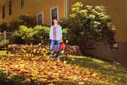Photo of person using Craftsman leaf blower SKU CMCK197M1 in a yard with scattered autumn leaves, yellow house in background.