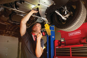 Photo of person working under a lifted car using a CRAFTSMAN cordless light, SKU CMCL020B, in a garage setting.