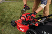 Photo of Craftsman V60 lawn mower CMCMW260P1, close-up of hands wearing gloves inserting battery on grass.