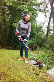 Photo of person using CRAFTSMAN string trimmer CMCST920B outdoors, trimming grass by a garden edge in a yard.