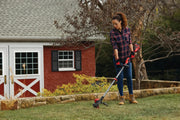 Photo of person using Craftsman CMCST920M1 string trimmer in garden near red shed, holding tool over grass.