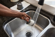 Person rinsing a vacuum filter at a kitchen sink with running water.