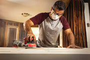 Photo of person using Craftsman cordless sander CMCW220B on a wooden surface in an indoor workspace.