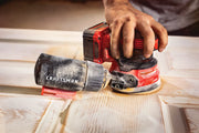 Photo of a Craftsman cordless random orbit sander being used on a wooden door, close-up side view.