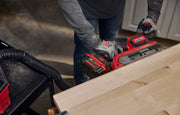 Photo of person using CRAFTSMAN cordless belt sander, SKU CMCW223B, sanding a wooden surface in a workshop.