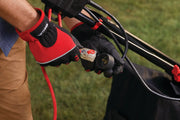 Close-up of a person wearing red and black gloves plugging a power cord into a CRAFTSMAN electric lawn mower. The mower is outdoors on green grass.