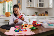 Photo of Craftsman CMGL100B cordless glue gun used for crafting, surrounded by colorful pom-poms on a kitchen table.