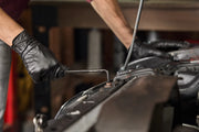 A person wearing black gloves uses a CRAFTSMAN hex key to work on a bolt under the hood of a car in a workshop setting.
