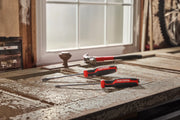 Three CRAFTSMAN hand tools, including two screwdrivers and a pry bar, are placed on a weathered wooden workbench. A hammer is also visible in the background near a window.