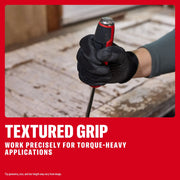 Gloved hand holding a screwdriver with a textured grip, suitable for precise, torque-heavy work on a wooden surface.