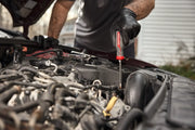 A person wearing black gloves is using a CRAFTSMAN screwdriver to work on the engine of a car.