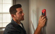 Photo of Craftsman CMHT77620 stud finder held against a gray wall by a person wearing a dark shirt.