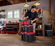 Photo of a person moving a stack of CRAFTSMAN tool boxes, SKU CMMT45242, with red lids and black bodies in a workshop.