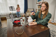 A person is repairing a white table lamp on a wooden table using hand tools from a CRAFTSMAN toolbox. Several screwdrivers