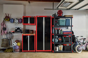 A garage storage system featuring Craftsman cabinets and shelving units in red and black. The area includes a tall cabinet, a smaller cabinet, a wall-mounted cabinet, and a multi-tier shelving unit holding storage bins and various items. Nearby, there are sports equipment, helmets, balls, and a children's bicycle visible.