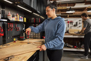 Two people working in a well-organized workshop. The person in the foreground is using a screwdriver on a piece of wood