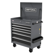 A gray Craftsman rolling tool chest with an open top compartment, six drawers, and four caster wheels for mobility. The tool chest has handles on the sides and a Craftsman logo on both the inside lid and front. There is also a side accessory tray attached.