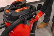 A person wearing red and black work gloves is handling a red CRAFTSMAN shop vacuum with a black hose, standing on a concrete floor.