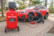 Photo of CRAFTSMAN CMXECXM331 air compressor with a red tank and black top, shown inflating a car tire outdoors.