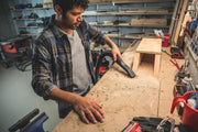 Photo of person using CRAFTSMAN CMXEVBE17584 wet/dry vacuum to clean dust on a woodworking bench in a workshop.