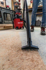 Photo of Craftsman wet/dry vacuum CMXEVBE17590 cleaning sawdust from a workshop floor, vacuum nozzle in focus.