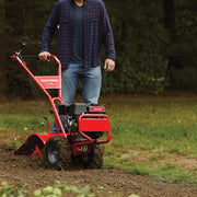 Photo of person using Craftsman tiller CMXGVAM1144037 in a garden, red frame and dirt-covered wheels visible.