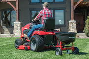 Photo of a Craftsman lawn tractor towing a Craftsman spreader, SKU CMXGZBF7124571, on grass in front of a house.