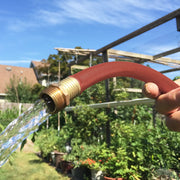 Photo of Craftsman garden hose CMXMHHF5850RL with brass fitting spraying water outdoors in garden setting.