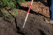 Photo of CRAFTSMAN garden hoe, SKU CMXMLTP35319, digging in soil outdoors near plants and mulch.