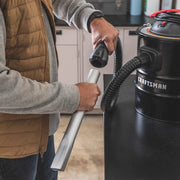 Photo of a person connecting a hose attachment to a Craftsman ash vacuum, SKU CMXZVBE43268, in a workshop.